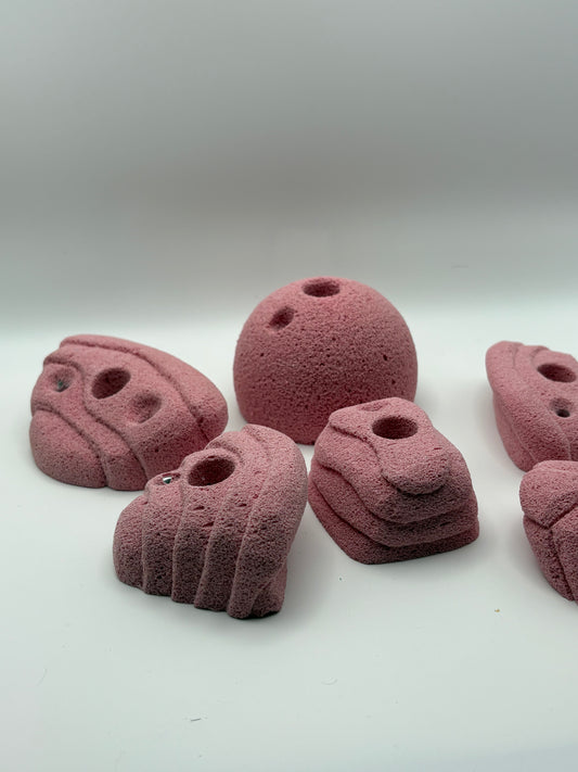 Set of pink resin climbing holds on white background